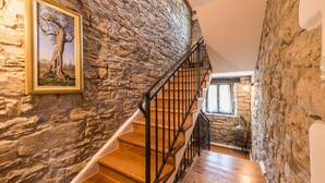 Un escalier avec des marches en bois et des rampes noires, menant à une pièce aux murs de pierre et dotée d’une fenêtre.