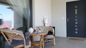 Un balcon avec des fauteuils en osier, une petite table et une porte blanche dotée d’une fenêtre.