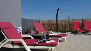 Un espace aménagé au bord de la piscine, avec des chaises longues, une table sur laquelle sont posées des bouteilles et un panneau indiquant la présence d’une piscine.
