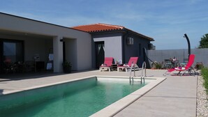 Une maison moderne dotée d’une piscine, de chaises longues rouges et d’un patio couvert.