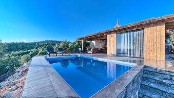A modern villa with a swimming pool, wooden deck, and a view of the surrounding hills.