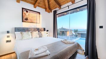 A bedroom with a large bed, a view of a pool and buildings, and a wooden ceiling.