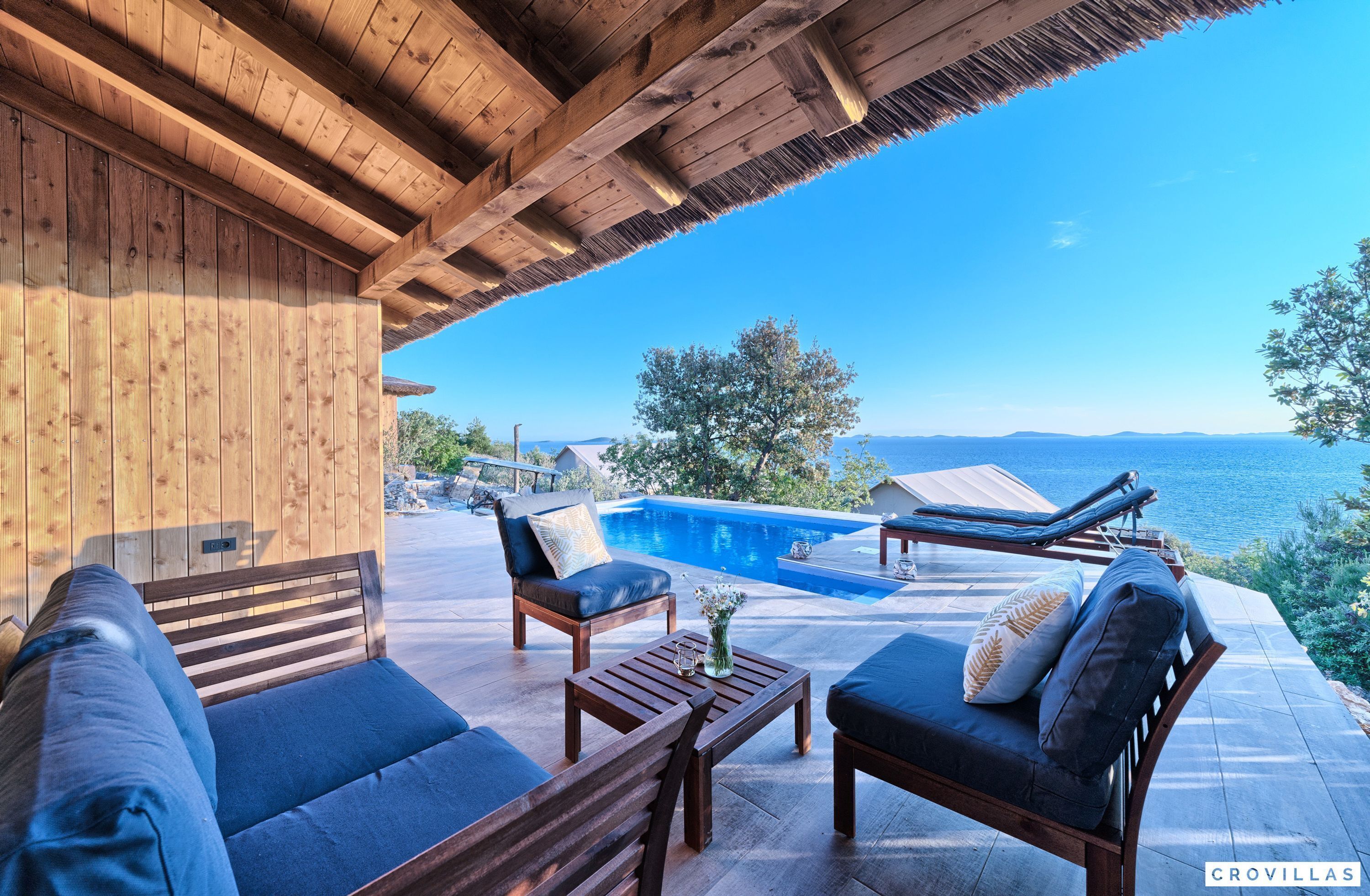 A wooden deck with a pool, lounge chairs, and a sofa.