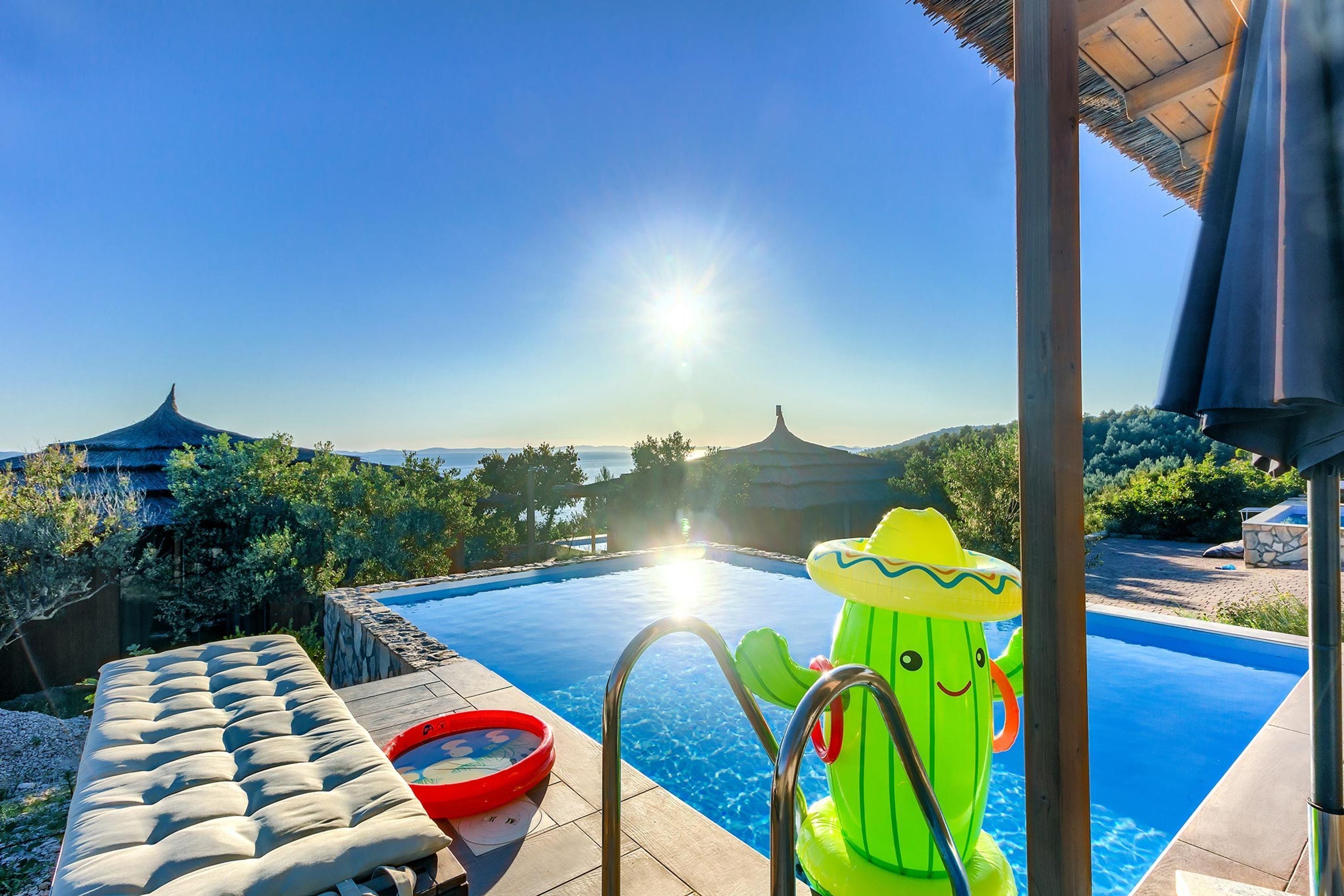 A pool with a clear view of the sea, a lounge area, and a cactus-shaped inflatable toy.