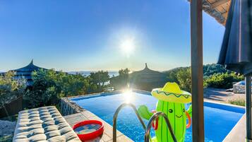 A pool with a clear view of the sea, a lounge area, and a cactus-shaped inflatable toy.