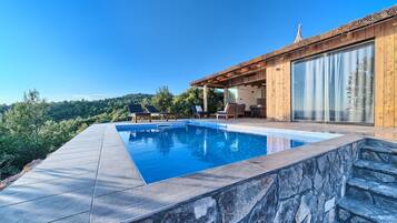 A modern outdoor pool area with a stone border, wooden deck, and lounge chairs.