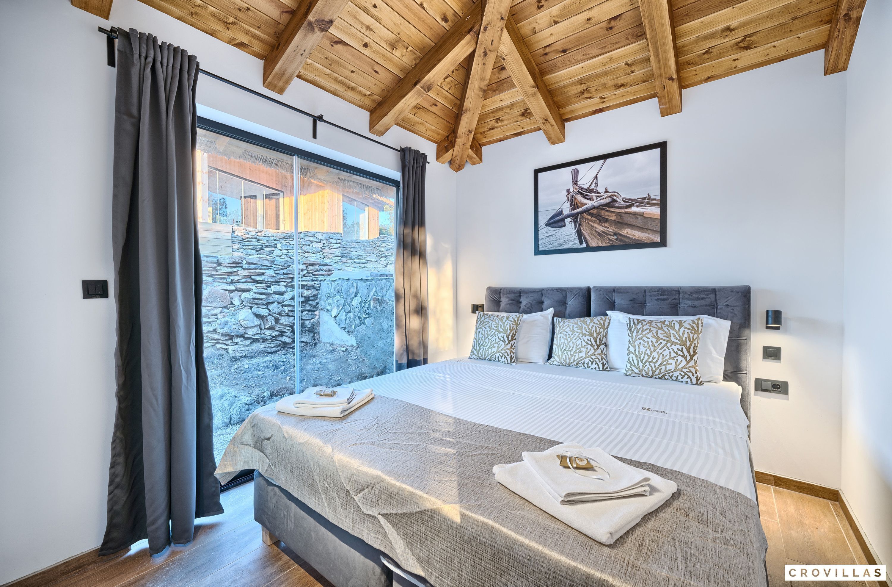 A bedroom with a large bed, a stone wall, and a wooden ceiling.