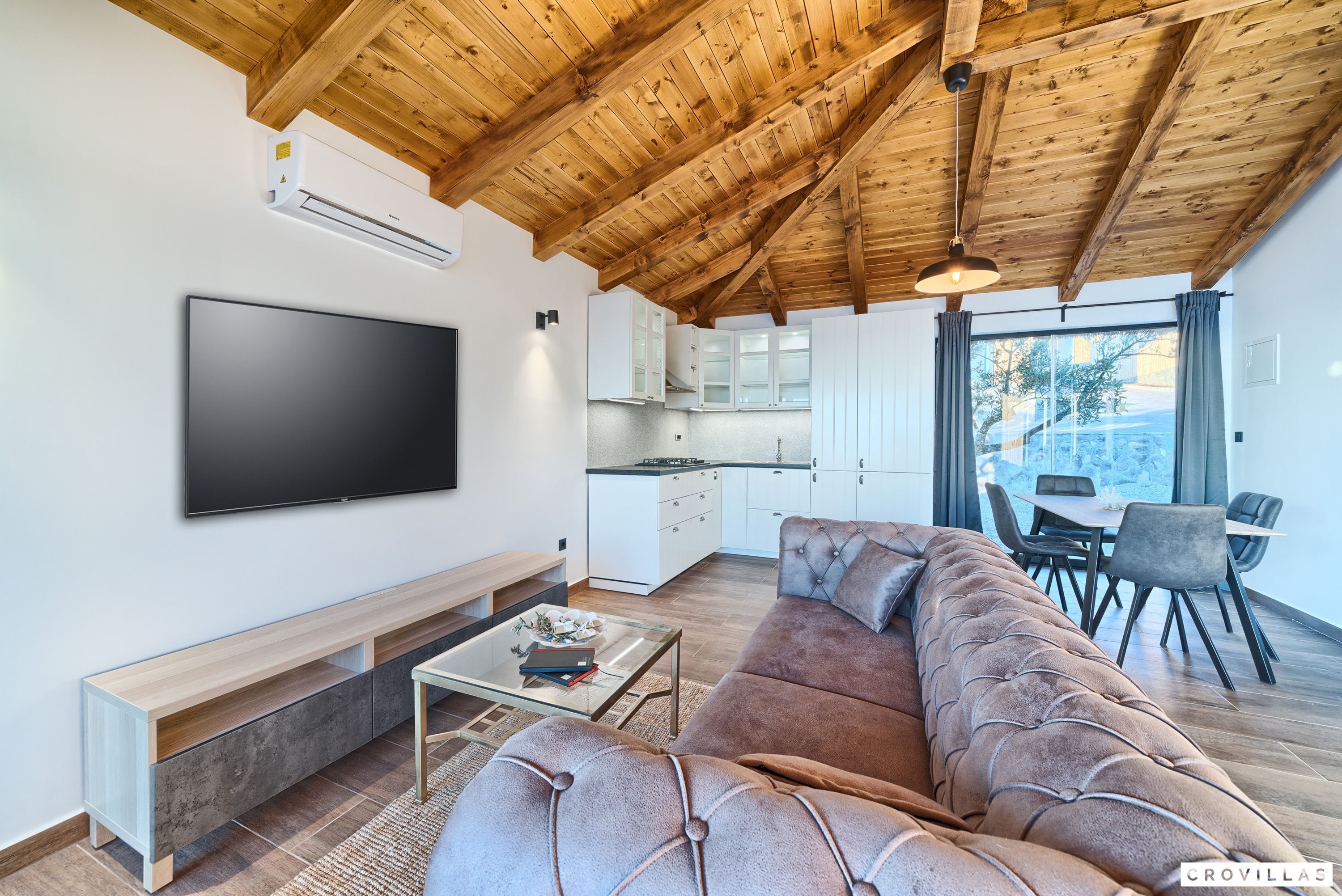 A modern living room with a large flat-screen TV, a sofa, a coffee table, and a wooden ceiling.