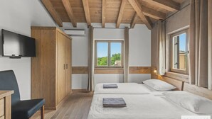 Ein Schlafzimmer mit zwei Betten, einer Holzbalkendecke, einem Fernseher und einem Fenster mit Ausblick.