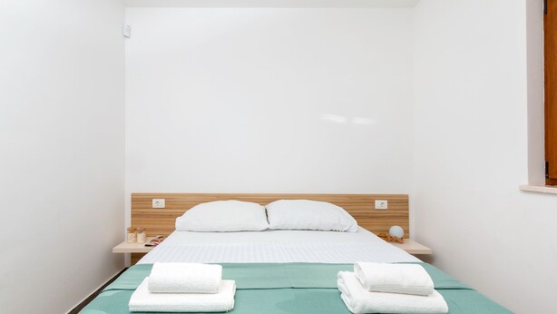 Ein kleines, sauberes Zimmer mit einem Bett, zwei Nachttischen und einem Fenster.