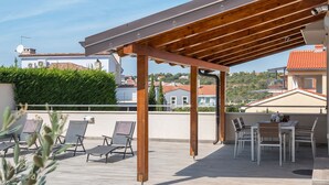 Eine Dachterrasse mit Holzpergola, Liegestühlen und einem Esstisch.