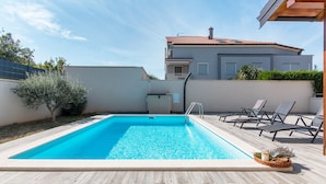 Ein rechteckiger Pool mit glasklarer, blauer Wasseroberfläche, umgeben von einer Holzterrasse.