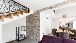 A modern living room with a purple sofa, a wooden staircase, a brick wall, and a dining area with a chandelier. - Grande Brscici in Svetvincenat (Svetvincenat)