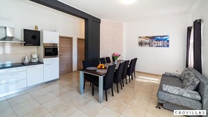 A modern kitchen with white cabinets, a dining table with black chairs, and a gray sofa. - Luce in Zadar With 4 Bedrooms and 4 Bathrooms (Benkovac)
