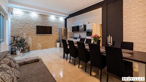 A modern living room with a sofa, dining table, and chairs, a kitchen in the background, and a stone wall. - Luce in Zadar With 4 Bedrooms and 4 Bathrooms (Benkovac)