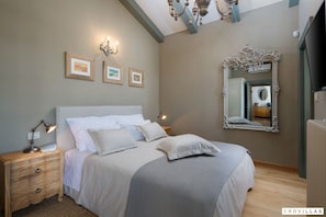 Quarto com cama, mesas de cabeceira, espelho e luzes na parede.