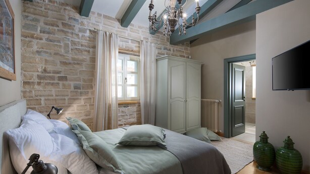 A bedroom with a stone wall, a bed with pillows, a wardrobe, a radiator, and a television. - Nevia in Ladi i With 5 Bedrooms and 5 Bathrooms (Kanfanar)