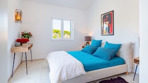 Un dormitorio con una cama, una ventana, una mesita de noche con lámpara y un cuadro en la pared.