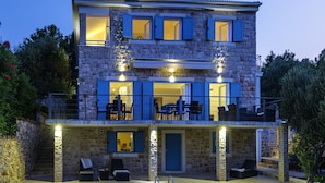 Una casa de piedra de dos plantas con balcón, mobiliario exterior e ingreso bien iluminado.