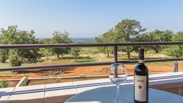 A table with a bottle of wine and a glass on a balcony overlooking a landscape with trees and a distant view. - Laura An in Dekli i (Kastelir-Labinci)