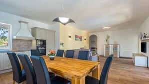 A modern kitchen with a wooden dining table and chairs, a built-in oven, and a large window. - Laura An in Dekli i (Kastelir-Labinci)