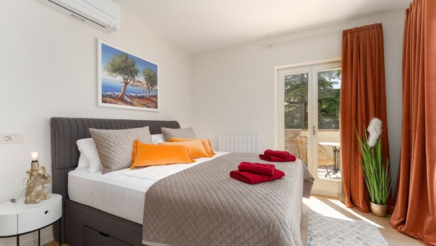 Een slaapkamer met een bed, een nachtkastje, een raam met gordijnen, een plant en een schilderij aan de muur.