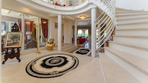 Een statig interieur met een wenteltrap, een grote kroonluchter en een rode bank op de bovenverdieping.