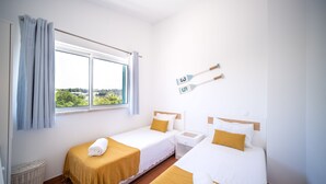 Een hotelkamer met twee bedden, een raam met gordijnen, een klein tafeltje en een mand.