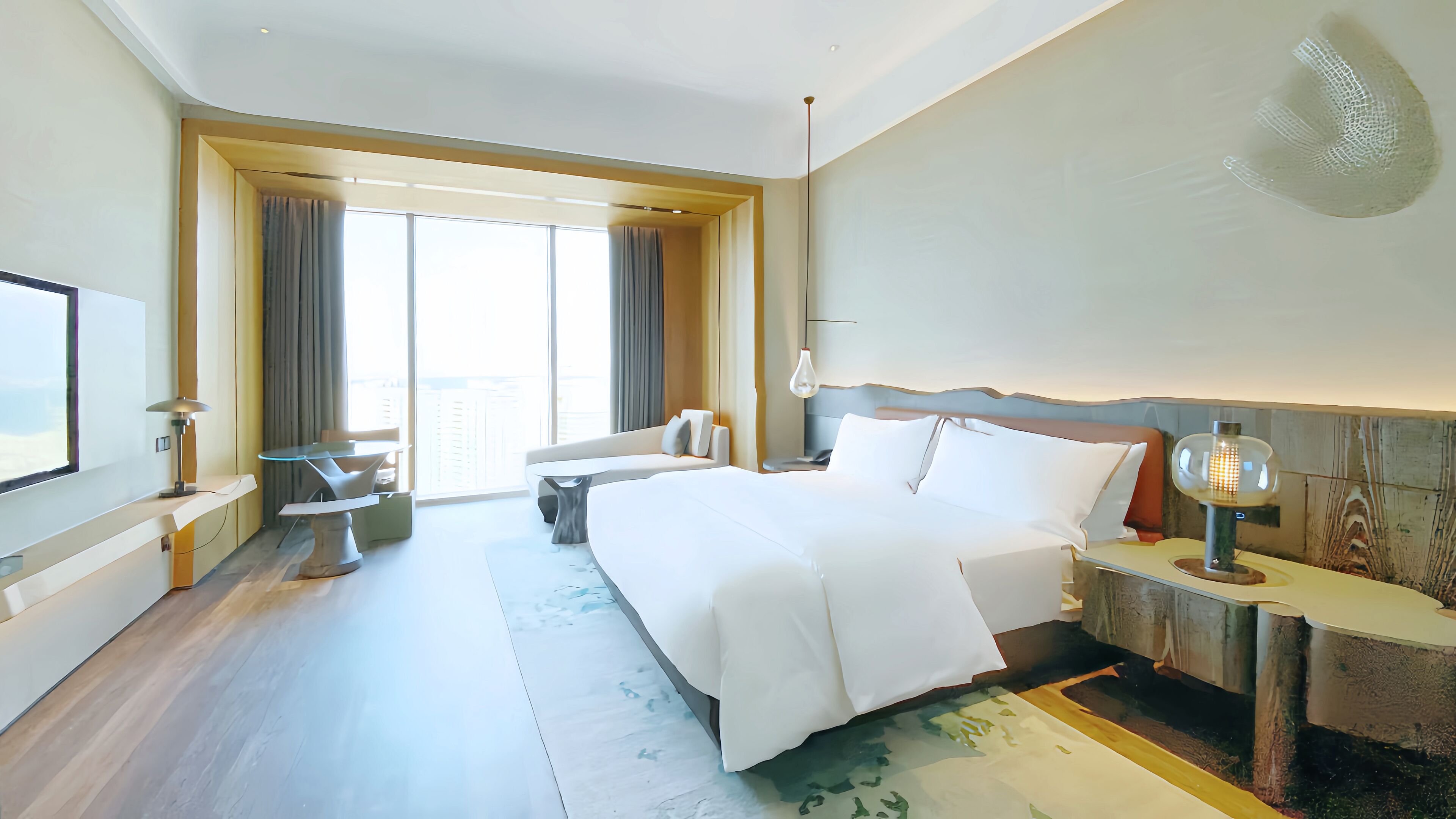 Habitación de hotel moderna con una cama grande, un escritorio, una silla y vistas a la ciudad a través de amplios ventanales.