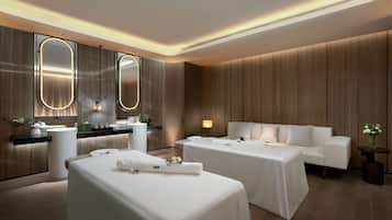 Two beds with crisp linens and pillows, a large mirror, and a small table with a vase of flowers.