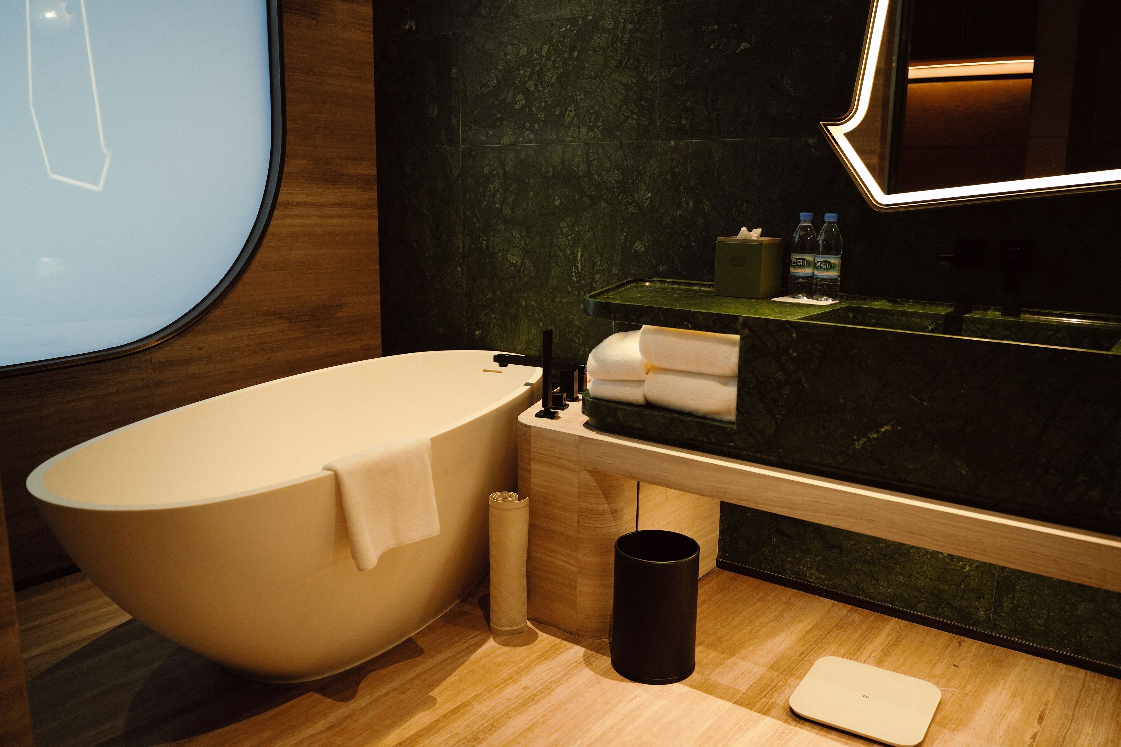Un baño moderno con una bañera independiente, un tocador de madera con espejo y un reverso de mármol verde.
