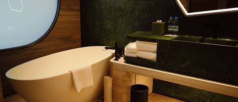 Un baño moderno con una bañera independiente, un tocador de madera con espejo y un reverso de mármol verde.