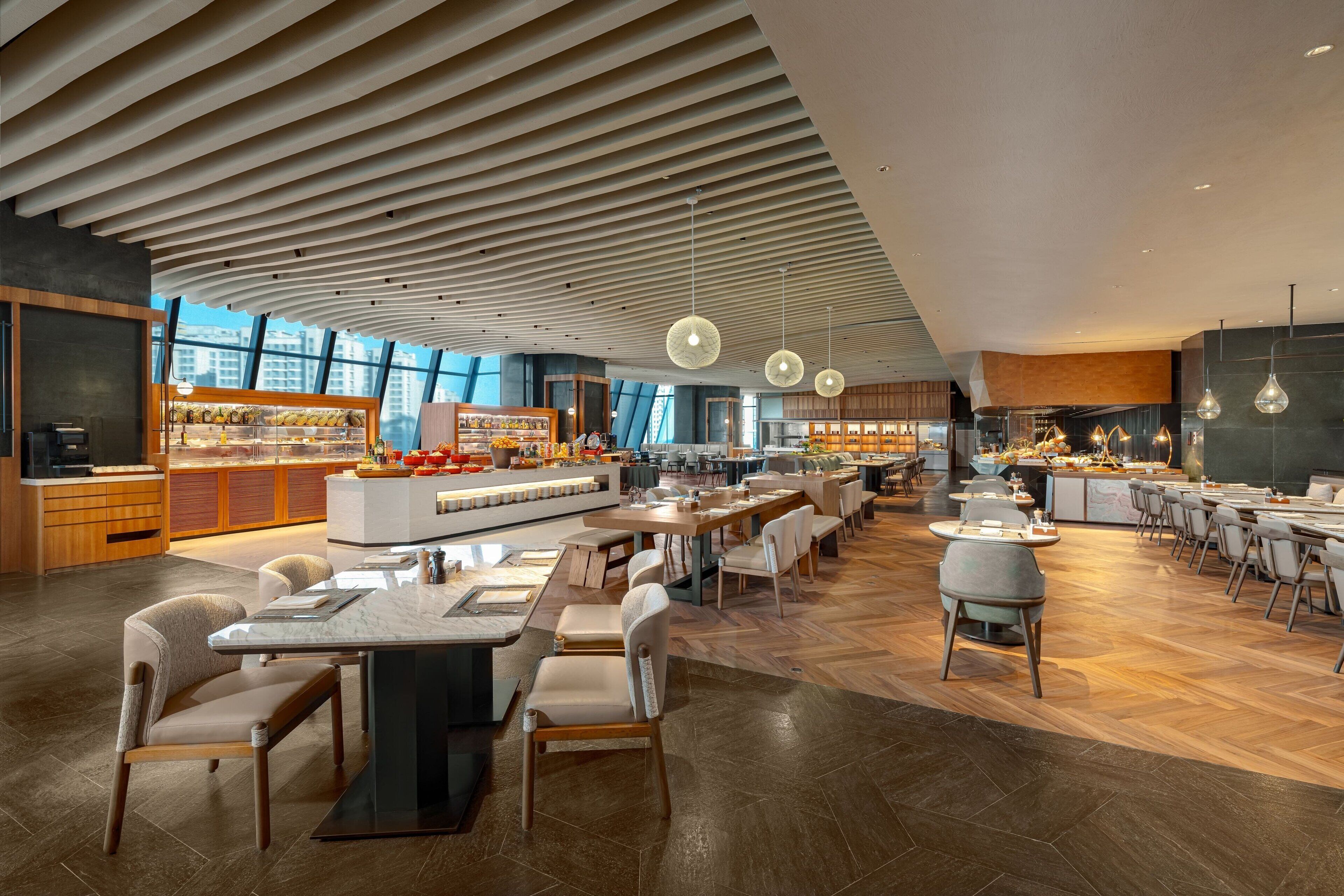 A spacious restaurant with a modern design, featuring a central bar area, multiple dining tables, and a high ceiling with unique lighting fixtures.