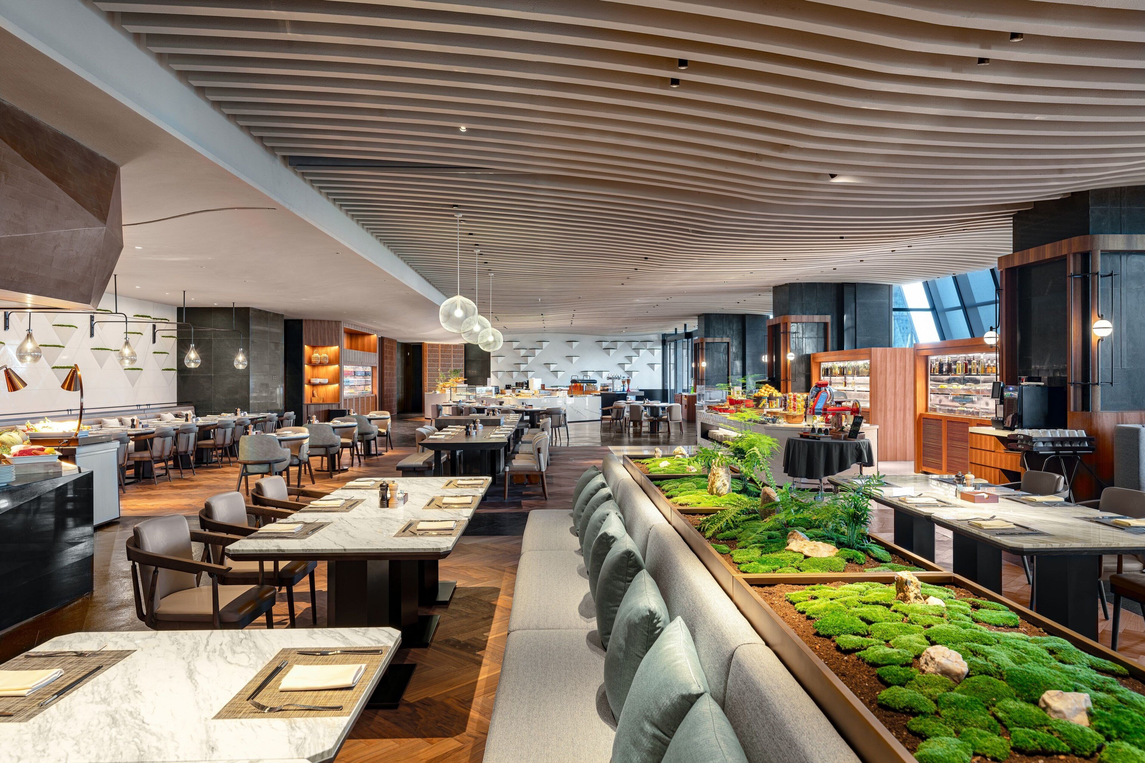A modern restaurant with a long counter, seating, and a ceiling with a unique design.