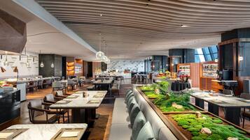 A modern restaurant with a long counter, seating, and a ceiling with a unique design.