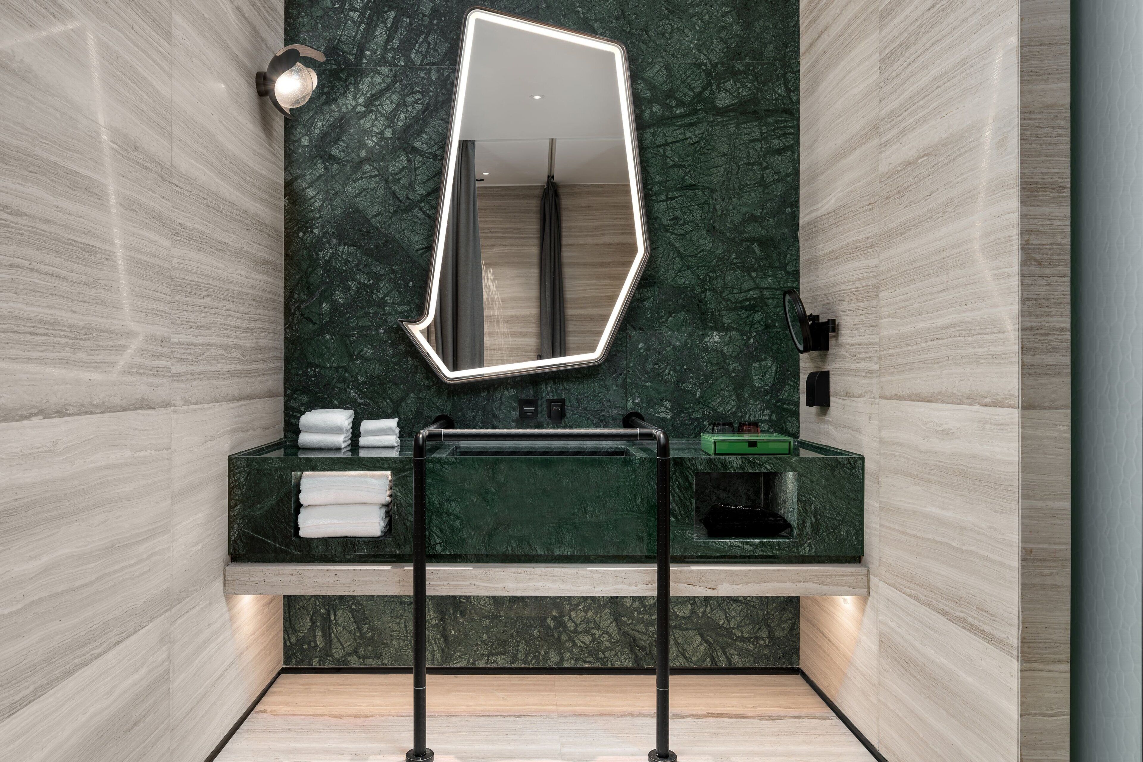 Un baño moderno con pared de mármol verde, un espejo grande y un lavabo con encimera verde.