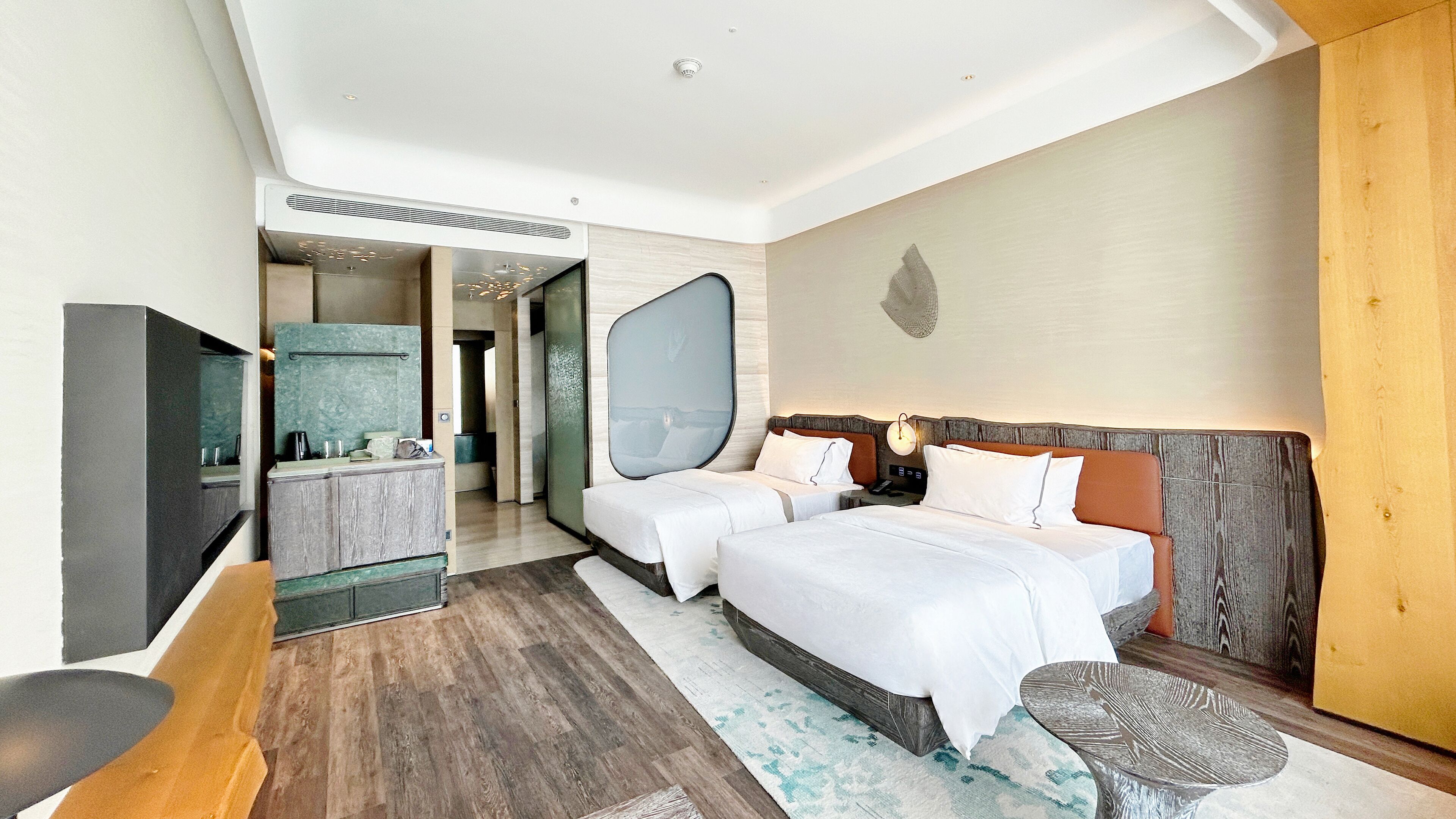 A modern hotel room with two beds, a large mirror, a vanity with a sink, and a television.