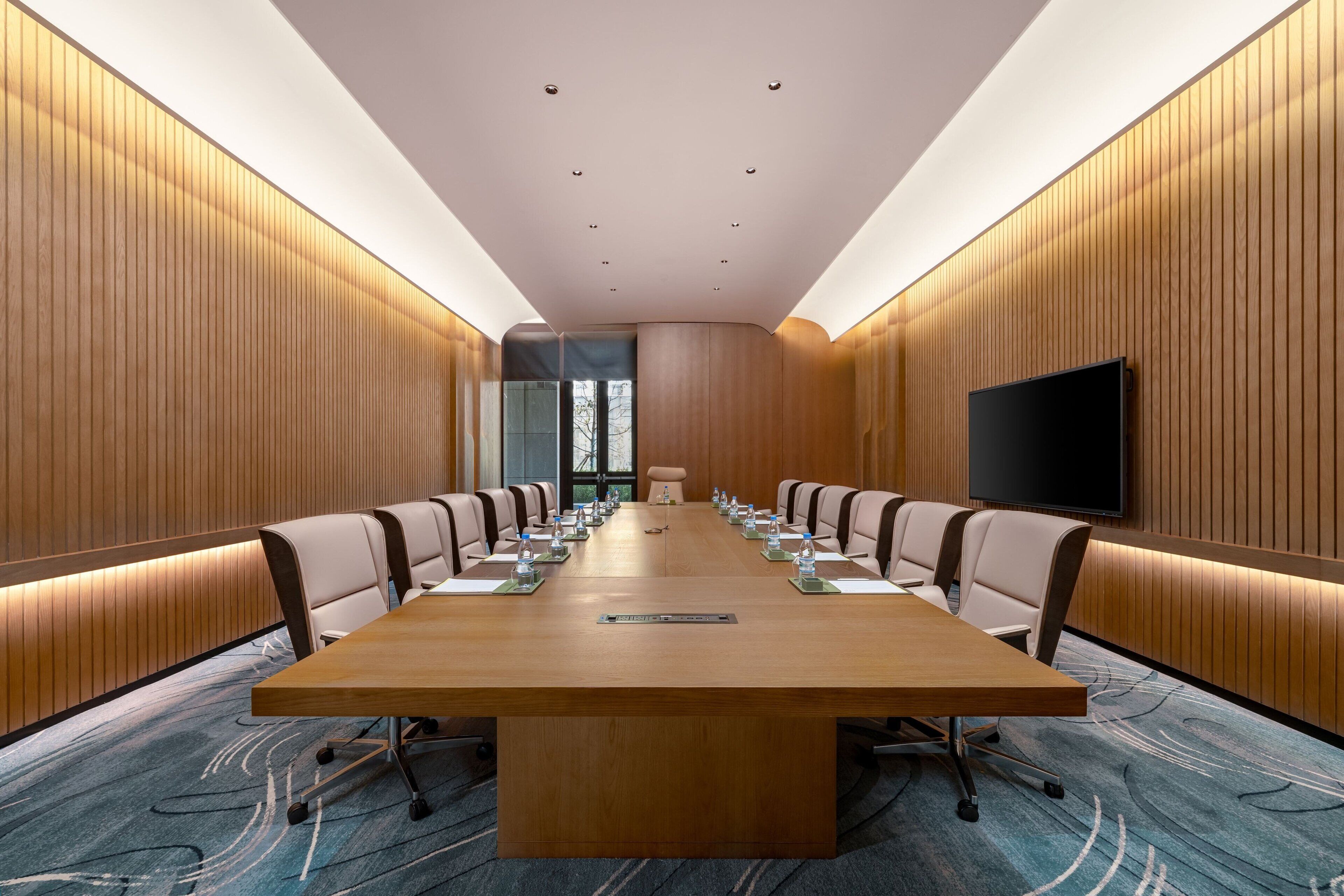 Une salle de conférence avec une longue table, des chaises, un téléviseur et un mur recouvert de panneaux de bois.