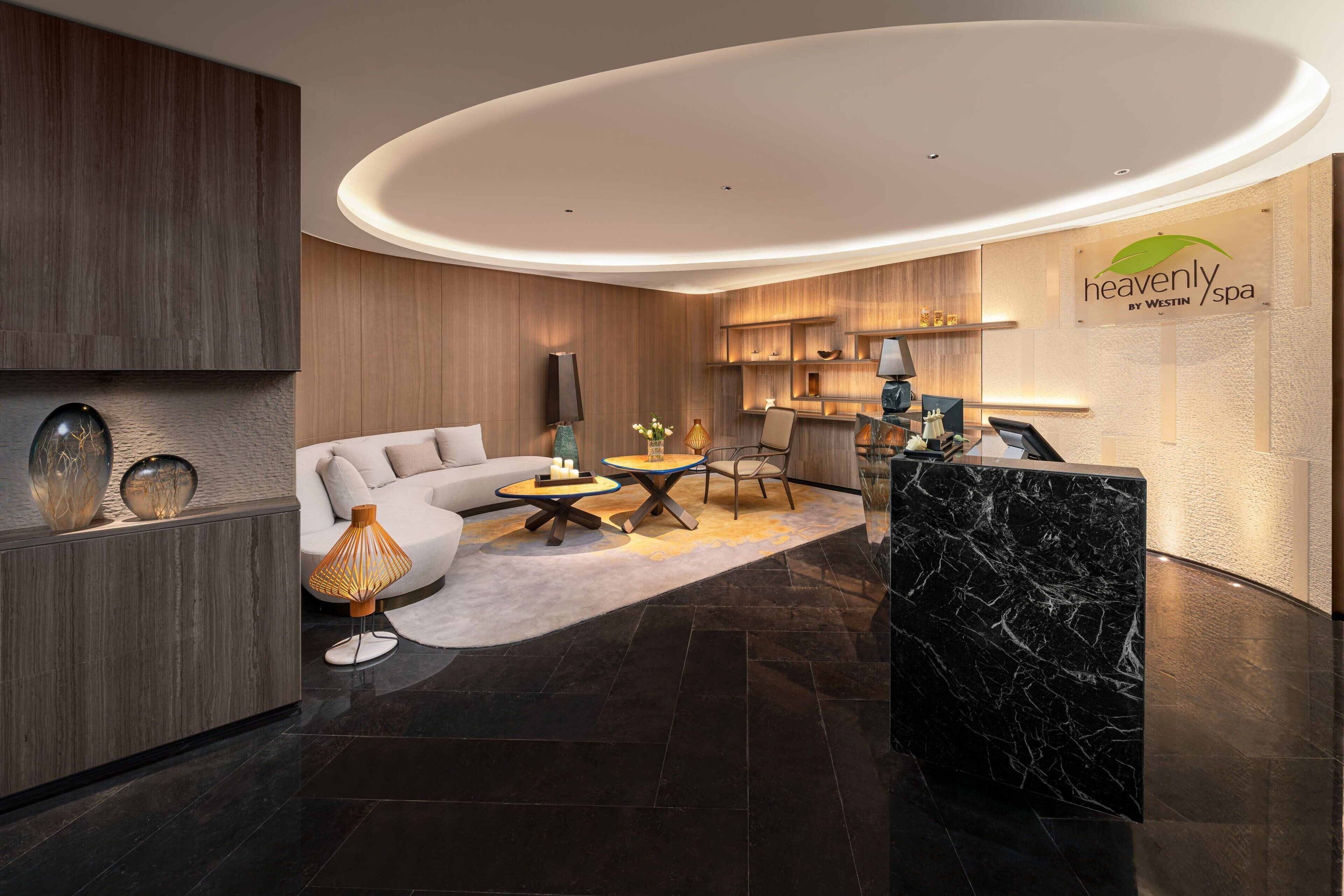Un espace d’accueil moderne doté d’un plafond incurvé, d’un comptoir de réception, d’un canapé et d’une table basse.