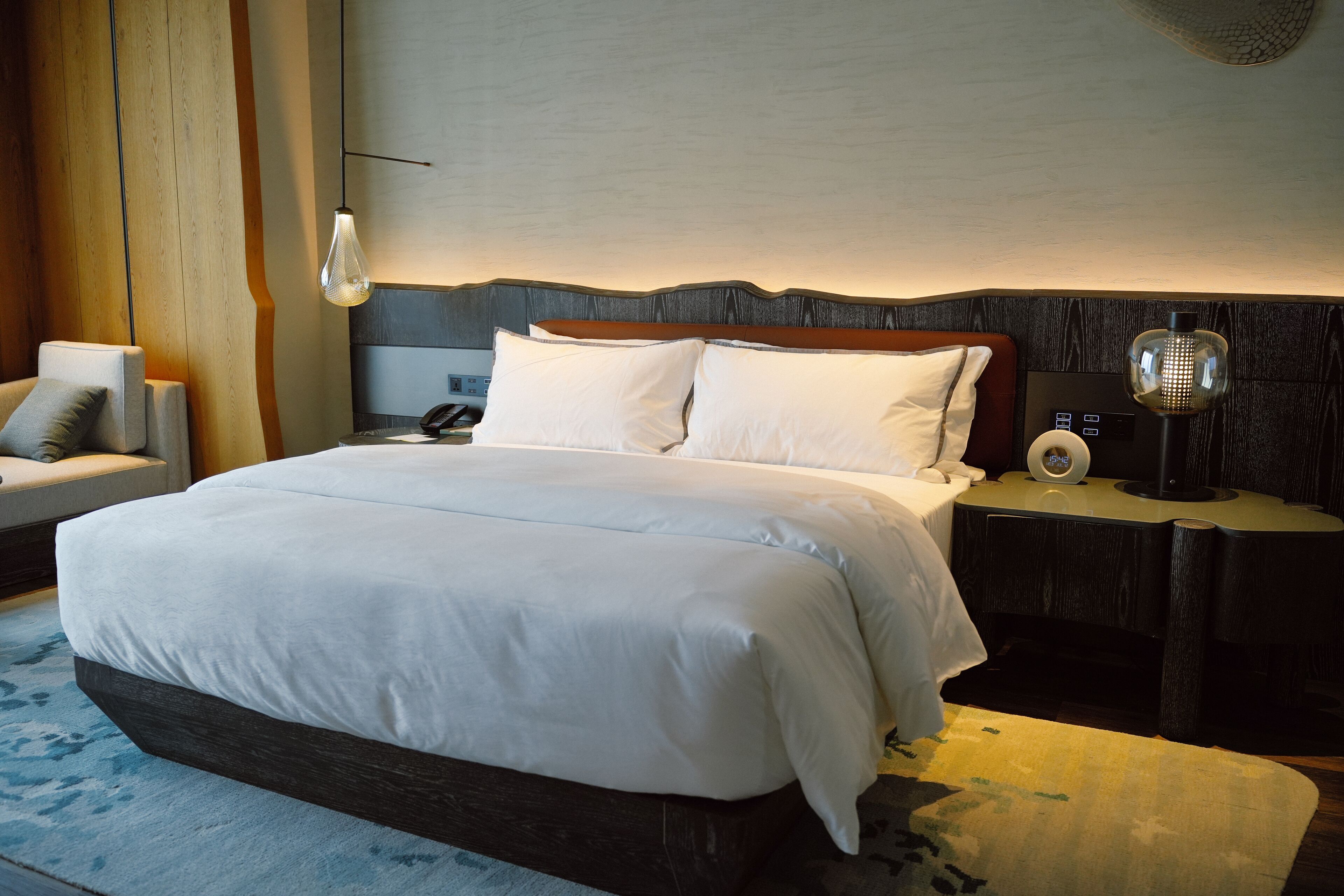 A modern hotel room with a large bed, a bedside table with a lamp, and a chair.