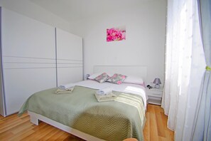 Een keurig opgemaakt slaapkamer met een bed, kussens, een nachtkastje en een aan de muur hangend schilderij.