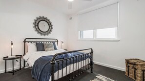 Een slaapkamer met een bed, nachtkastjes, een spiegel, een raam en een rieten mand.