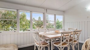A dining area with a table and chairs, large windows, and a view of greenery outside.