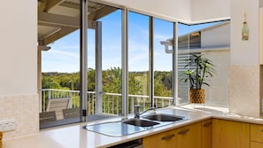 Cozinha moderna com uma janela ampla, pia e varanda com vista para o verde.