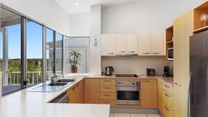 A modern kitchen with a large window, stainless steel appliances, and wooden cabinets. - Unit 6 'Sea Breeze Villas' (Coolum beach)