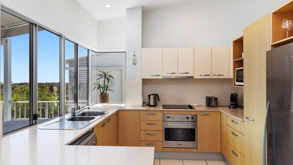 A modern kitchen with a large window, stainless steel appliances, and wooden cabinets. - Unit 6 'Sea Breeze Villas' (Coolum beach)