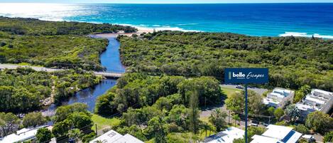 A residential area with a river, a bridge, and a beach in the background. There is a sign for 'Belle Escapes Property'.