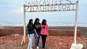Tre personer står foran et skilt, der siger 'Sandcastle Beach Resort'.
