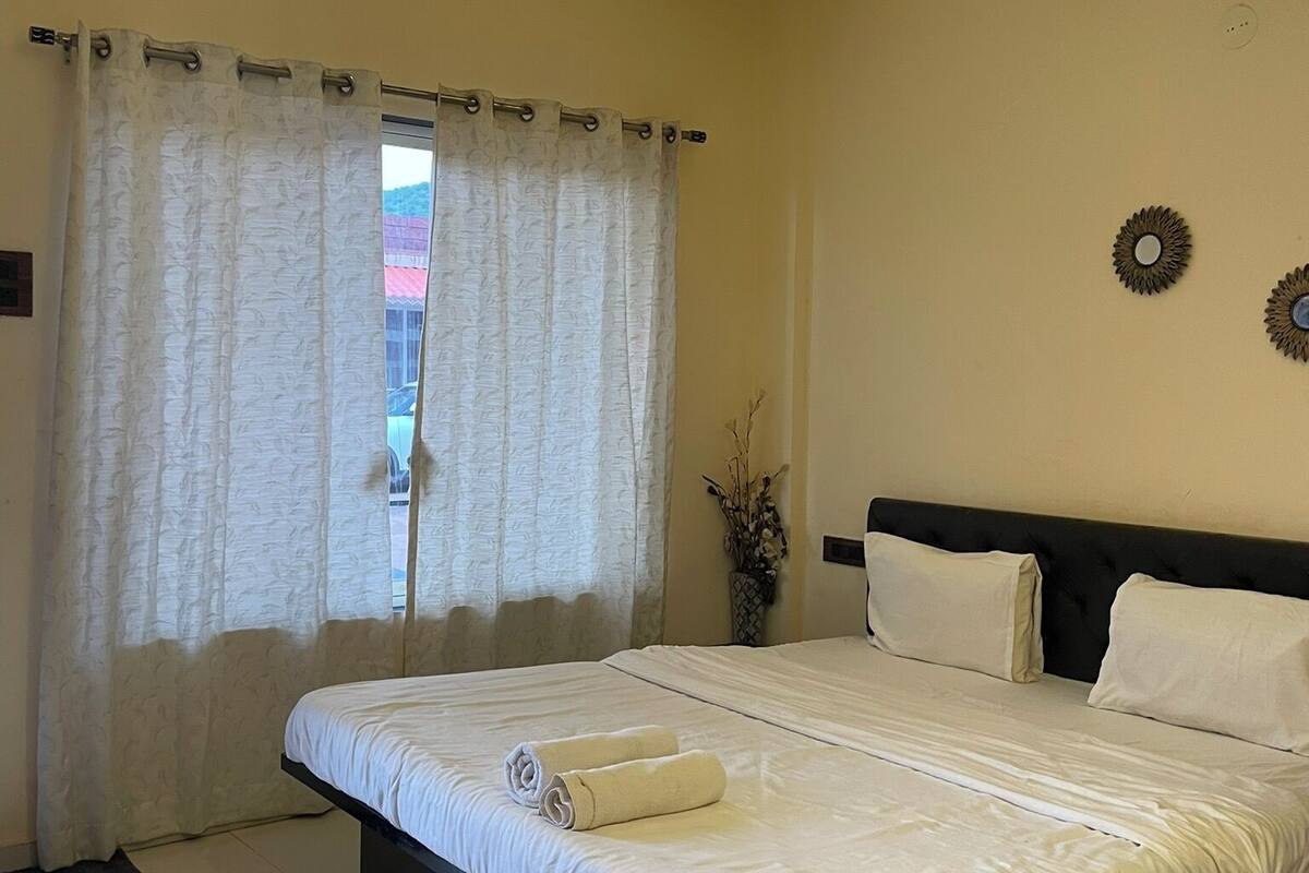 A bedroom with a bed, curtains, a ceiling fan, and a wall-mounted decoration.