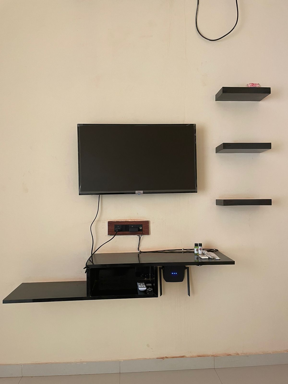 A wall-mounted TV with a flat-screen display, a wooden panel below, and a black entertainment unit with a remote control.